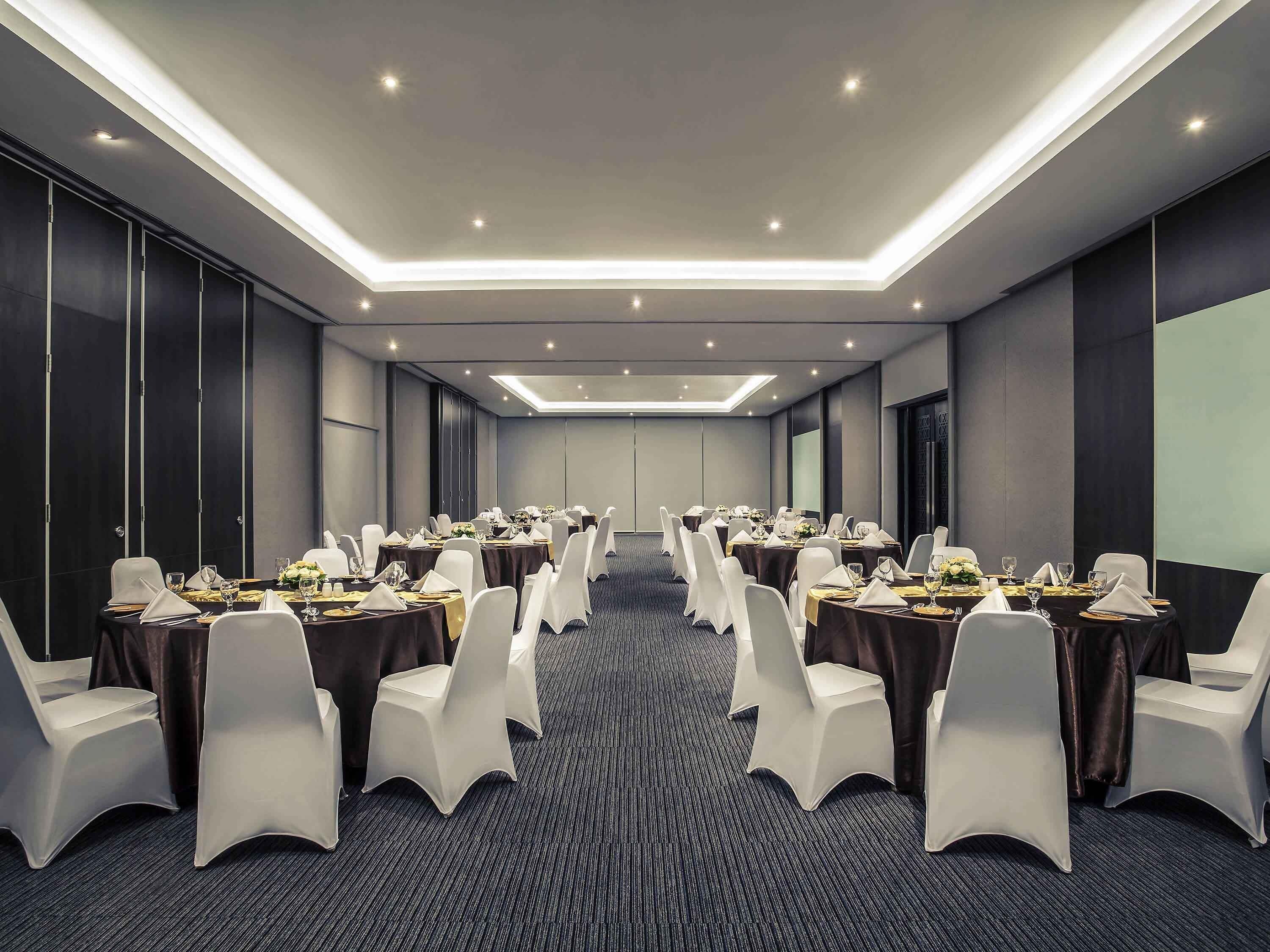 A conference room with round tables, white chairs, and a carpeted floor.