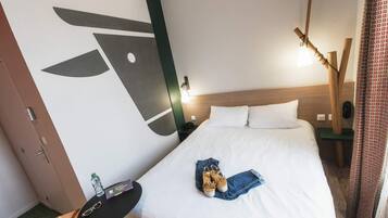 Quarto de hotel com uma cama, uma escrivaninha, uma cadeira e um enfeite de parede.