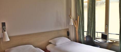 A hotel room with two beds, a desk with a laptop, a phone, and a lamp.