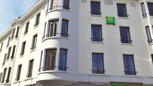 Een wit gebouw met veel ramen en balkons, een koepelvormige structuur linksboven, en een bord met de tekst 'ibis Styles' aan de rechterkant.