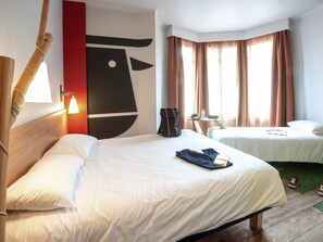 Ein Hotelzimmer mit zwei Betten, einem hölzernen Kopfteil, einem Wandbild, einem Nachttisch und einem Fenster mit Vorhängen.