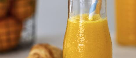 Una botella de vidrio con jugo de naranja y una pajita, un croissant, y un fondo borroso con una cesta de naranjas.