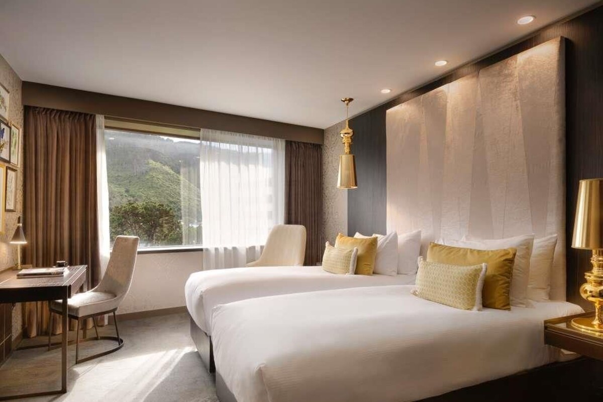 A hotel room with two beds, a desk, a chair, and a large window with curtains.