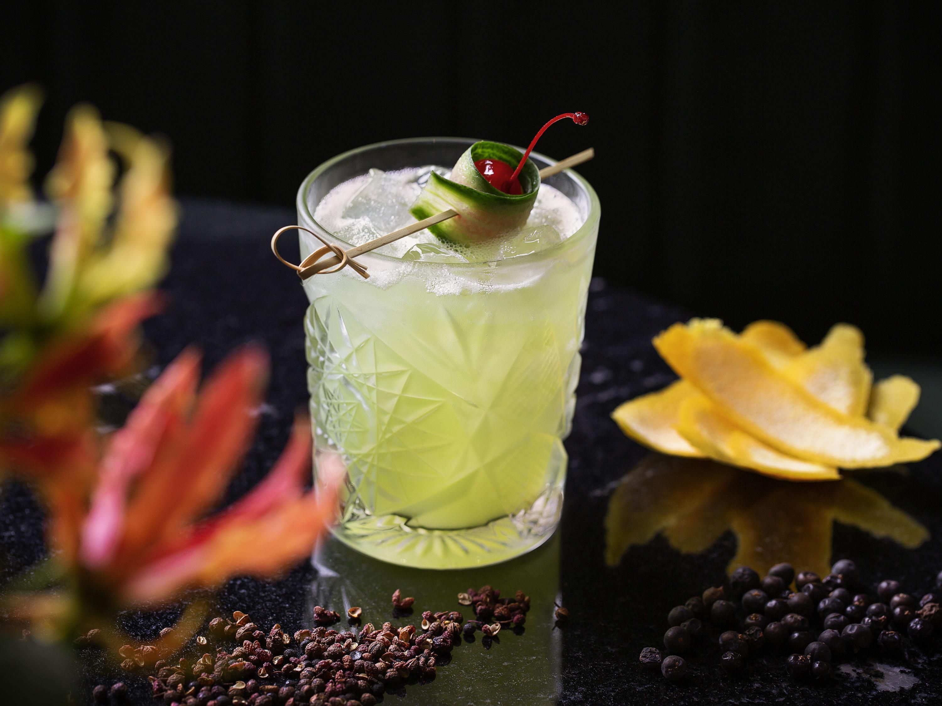 A cocktail glass with a lime garnish, surrounded by scattered spices and a flower.