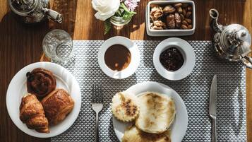 A breakfast setting with croissants, pastries, a teapot, a bowl of nuts, and a small vase with flowers on a wooden table.