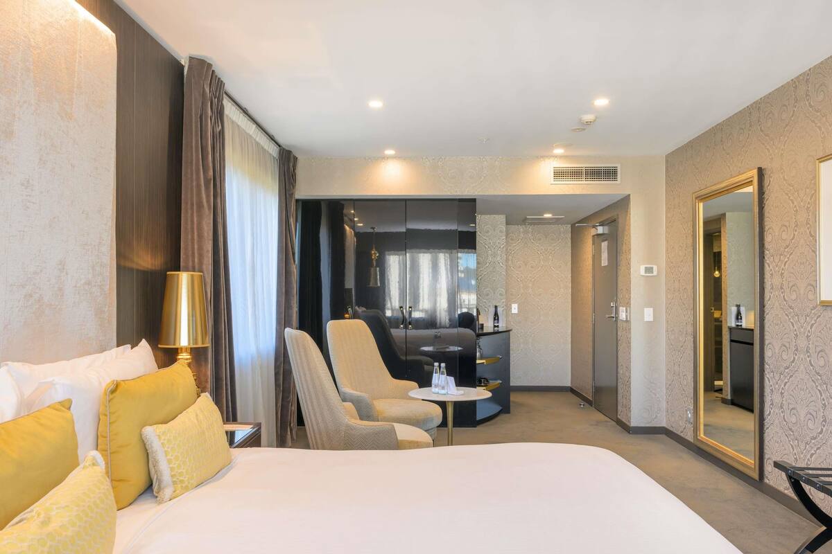 A hotel room with a large bed, a desk, a chair, and a mirror.