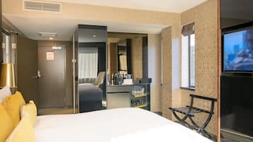 Habitación de hotel con cama, escritorio, silla, televisor y minibar.
