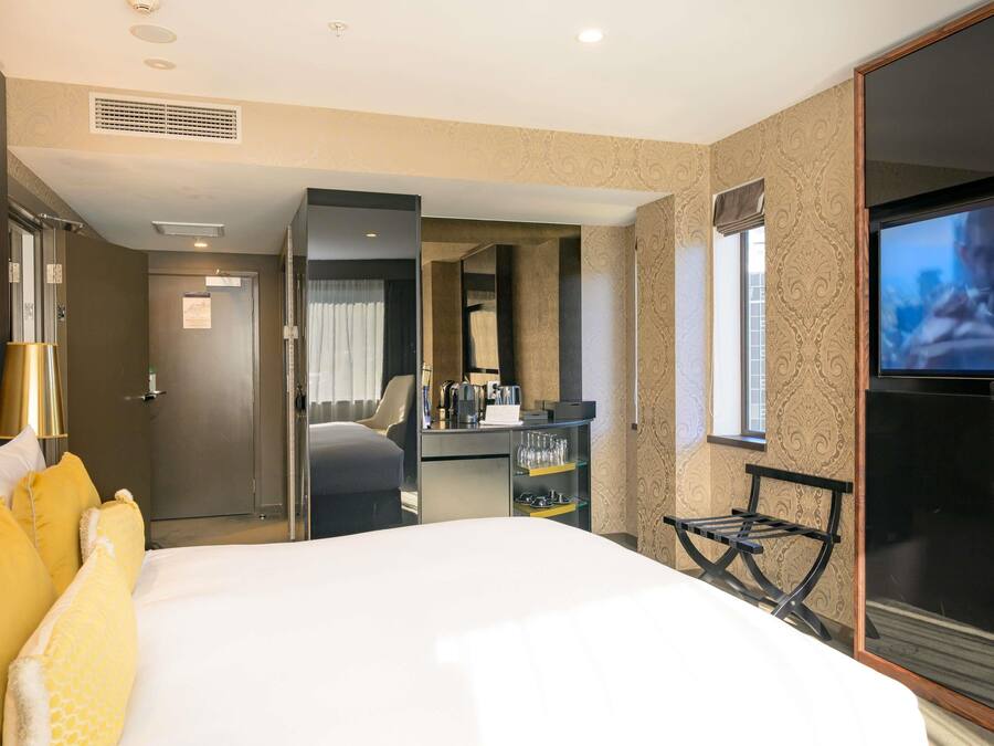 Habitación de hotel con cama, escritorio, silla, televisor y minibar.