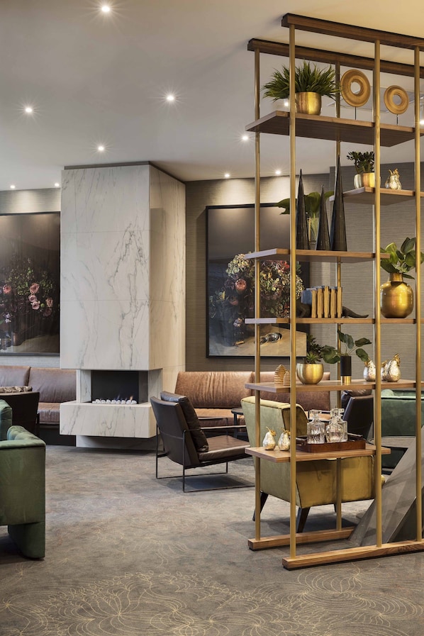 A modern living room with a marble fireplace, comfortable seating, and a decorative shelf with plants and vases. - Sofitel Wellington (Wellington)
