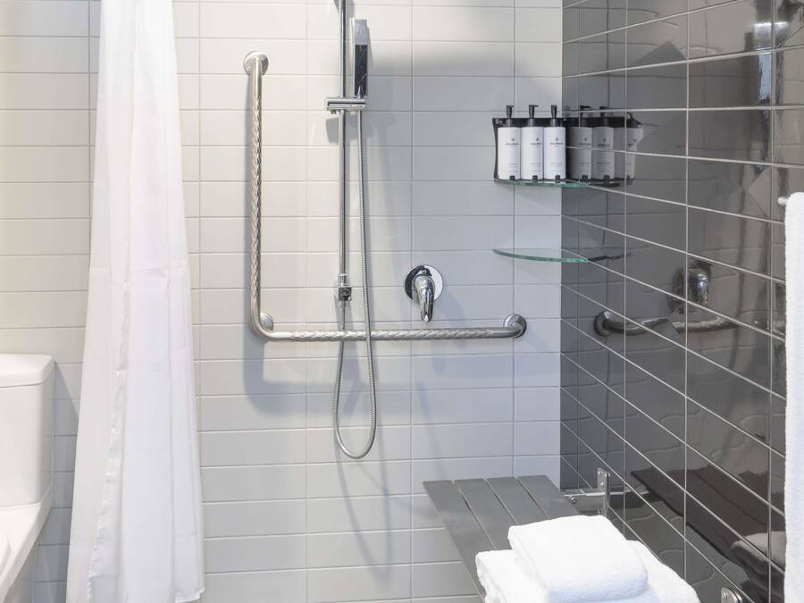A modern bathroom with a walk-in shower, grab bars, a glass shelf with toiletries, and a white towel on a metal rack.