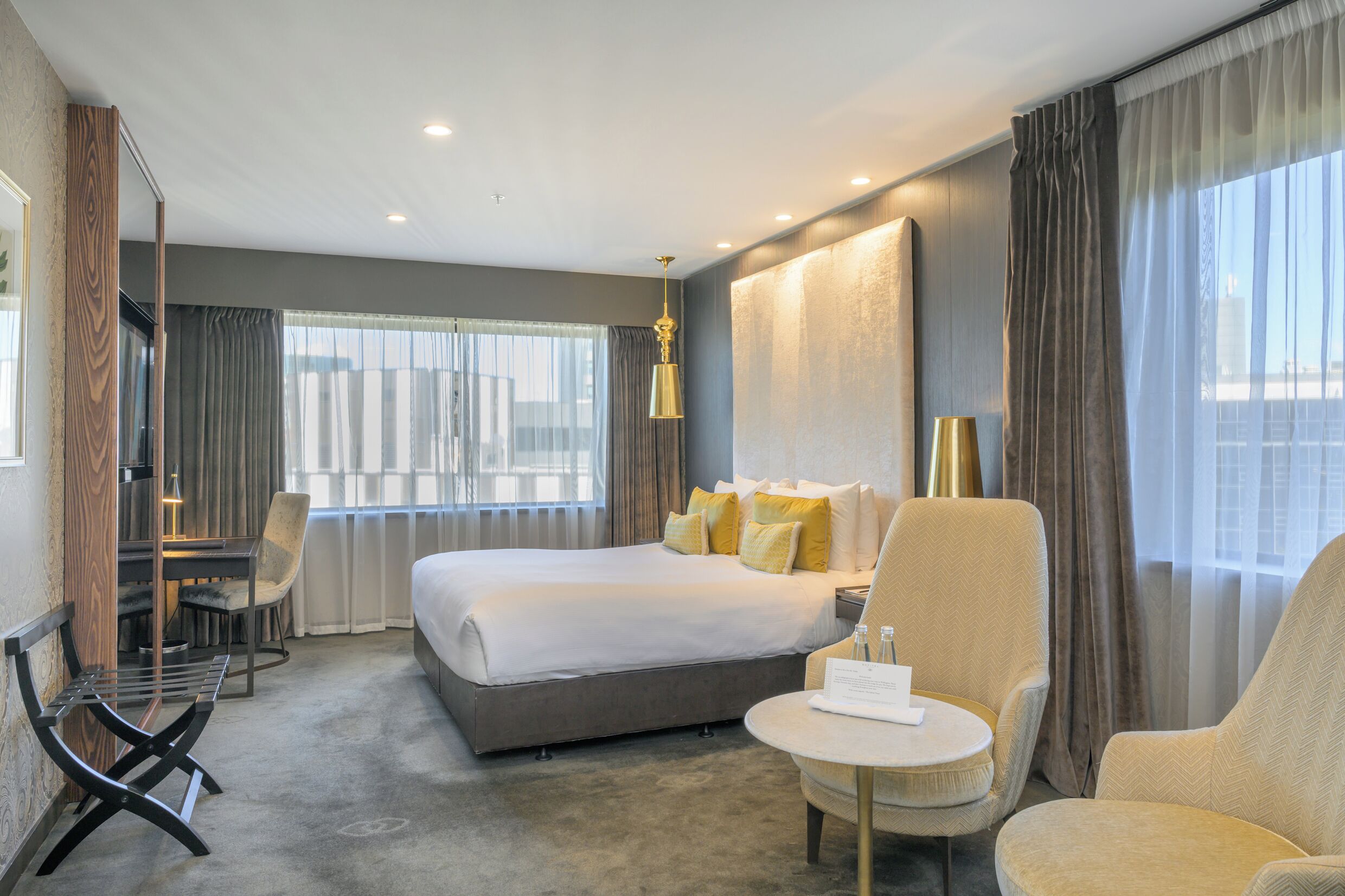 Ein modernes Hotelzimmer mit einem großen Bett, zwei Sesseln, einem kleinen Tisch und einem Schreibtisch mit Stuhl.