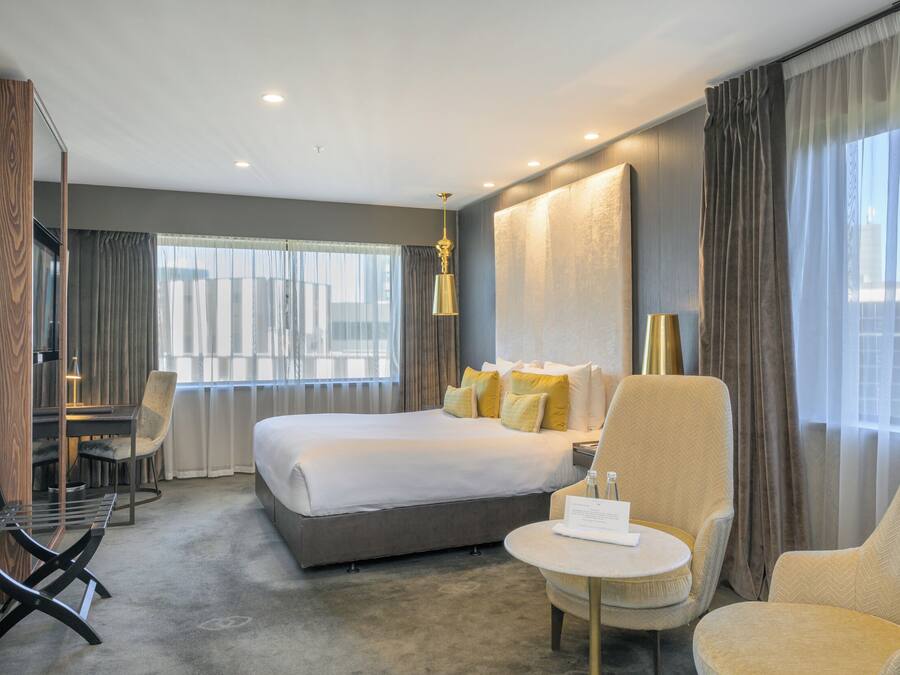 Habitación de hotel moderna con una cama grande, dos sillones, una mesita y un escritorio con una silla.