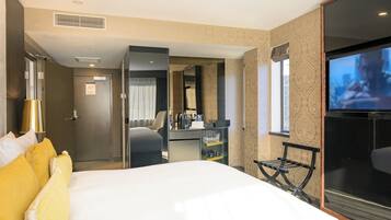 A hotel room with a bed, a desk with a chair, a TV, and a bathroom door.