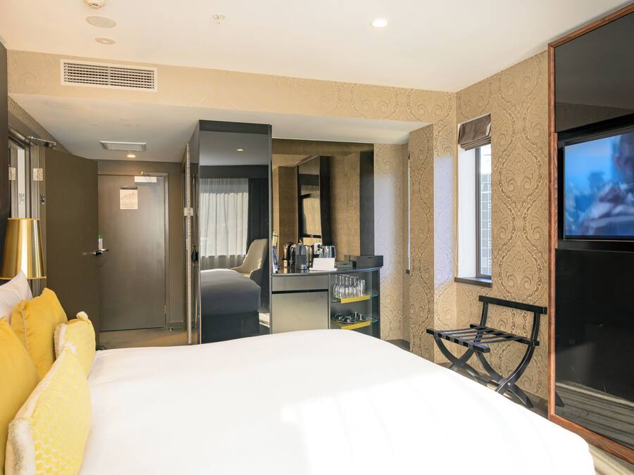 A hotel room with a bed, a desk with a chair, a TV, and a bathroom door.