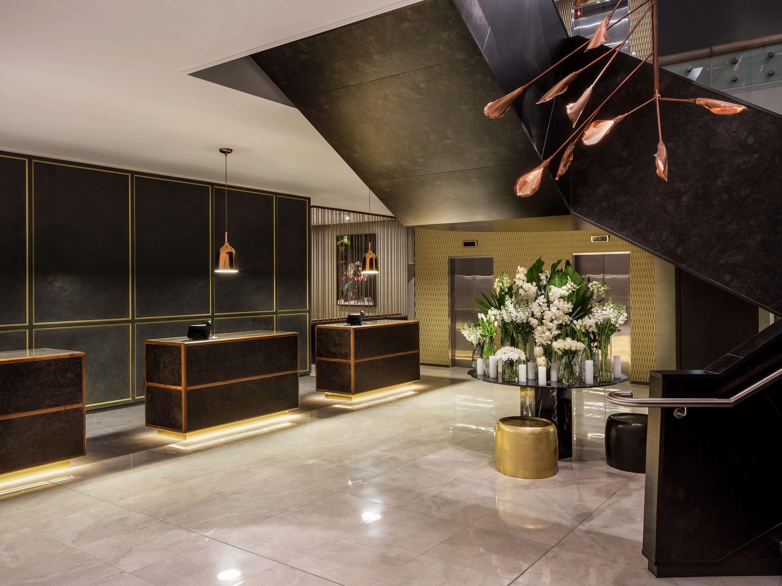A modern lobby with a reception desk, a staircase, and a floral arrangement.