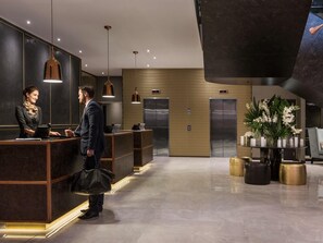 A hotel reception area with a modern design, featuring a reception desk, two elevators, and a decorative plant arrangement. - Sofitel Wellington (Wellington)