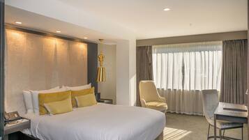 A hotel room with a large bed, a desk with a chair, a lamp, and a window with curtains.
