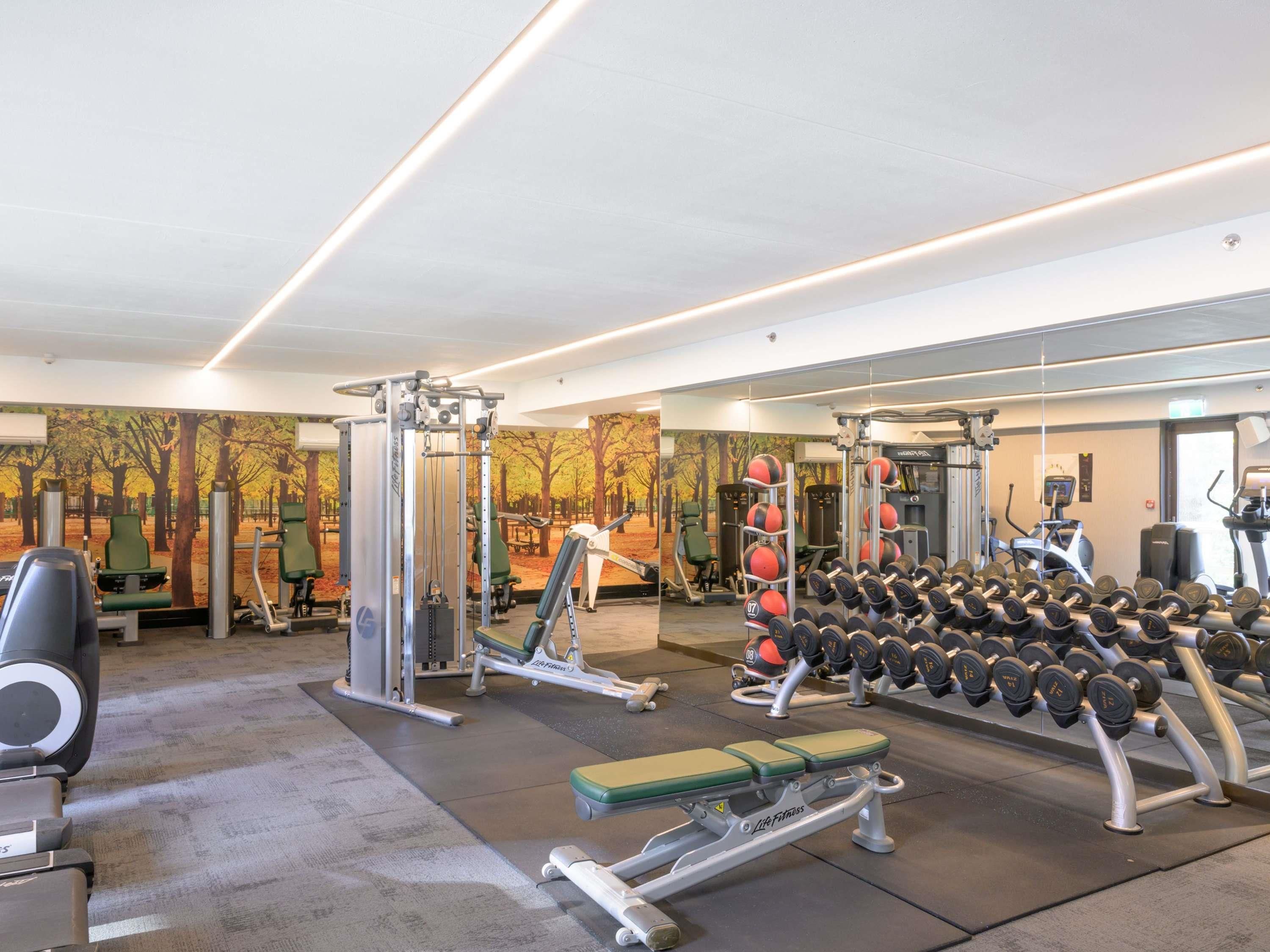 A gym with weightlifting equipment, benches, and a mirror wall.