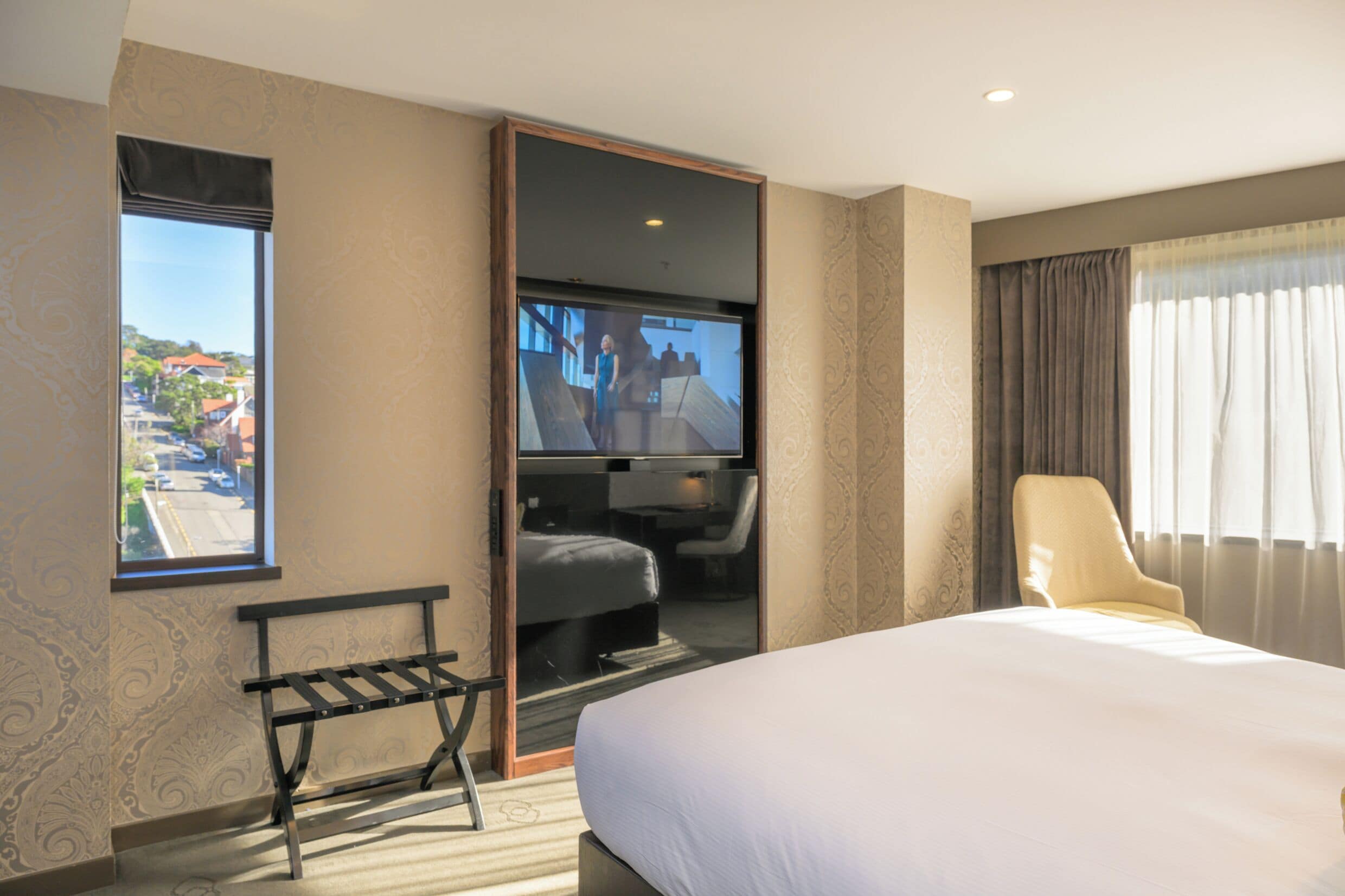 A hotel room with a large bed, a bench, a television, and a view of the outside.