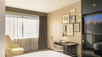A hotel room with a bed, a desk, a chair, a TV, and a window with curtains.