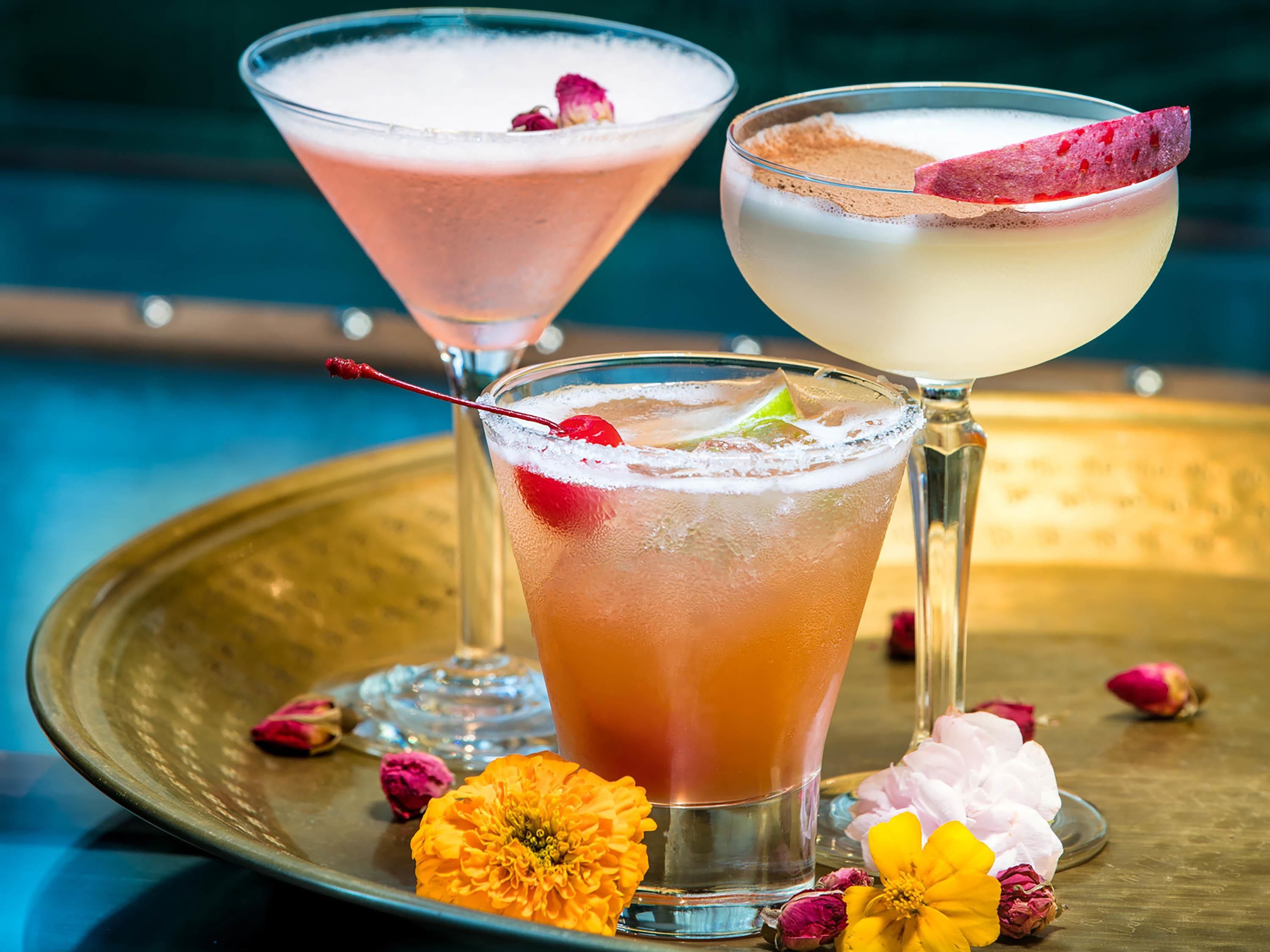 Three cocktails on a tray with flowers.