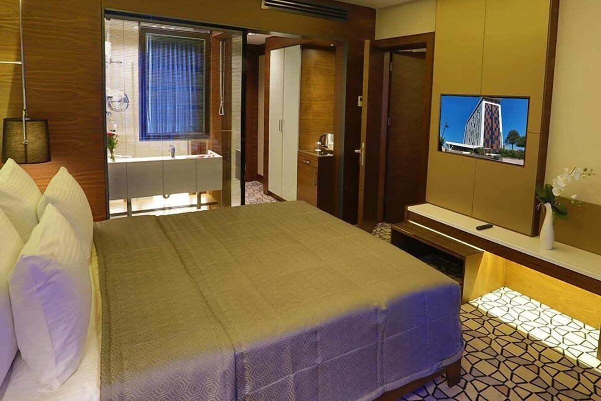 A hotel room with a bed, a bathroom, a TV, and a view of a building.