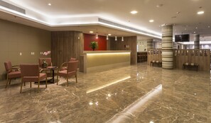 A hotel lobby with a reception desk, seating area, and a modern ceiling design.