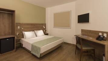 Habitación de hotel con cama, escritorio, silla, televisor y un refrigerador pequeño.