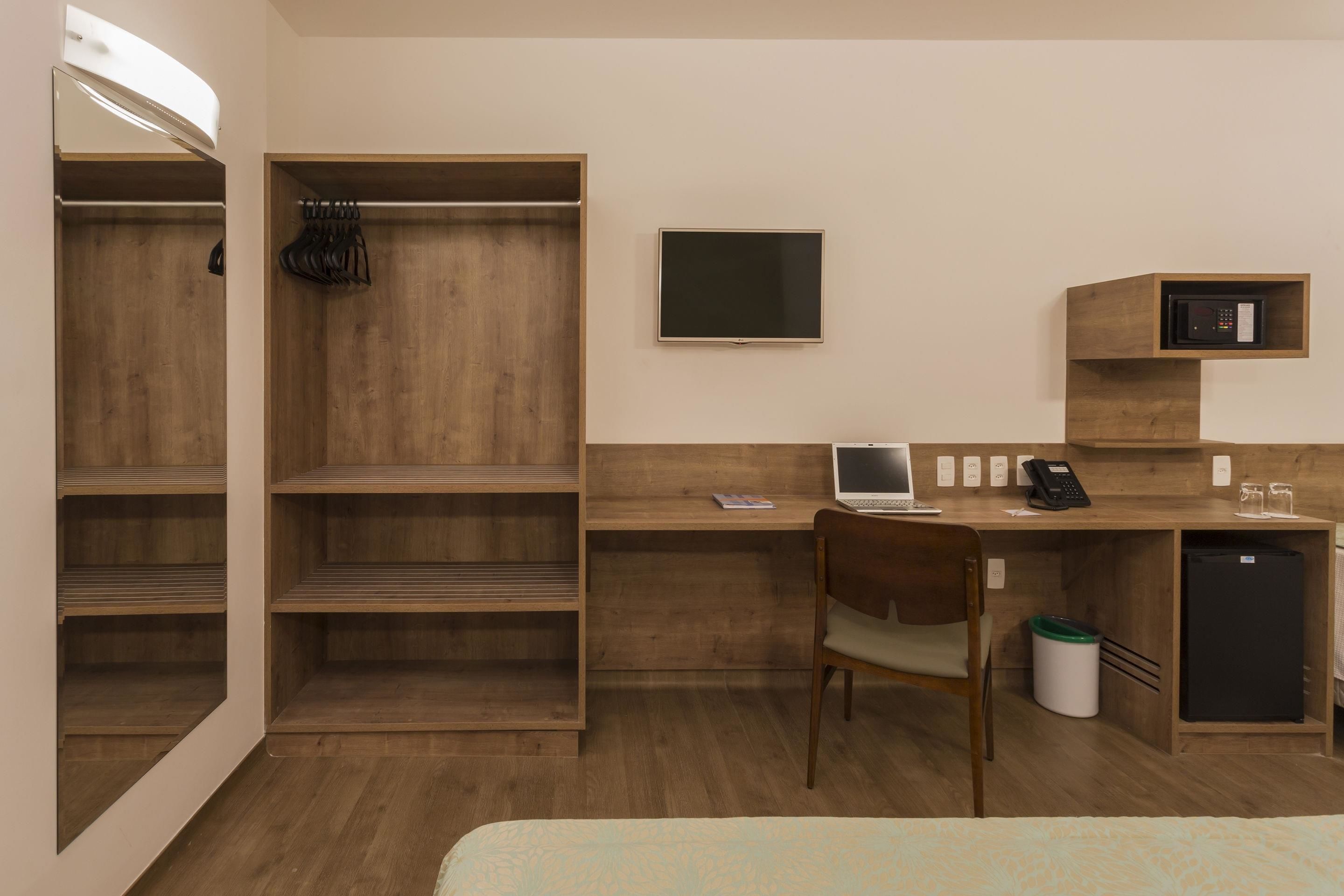 A hotel room with a wooden desk, a laptop, a television, a microwave, and a bed.