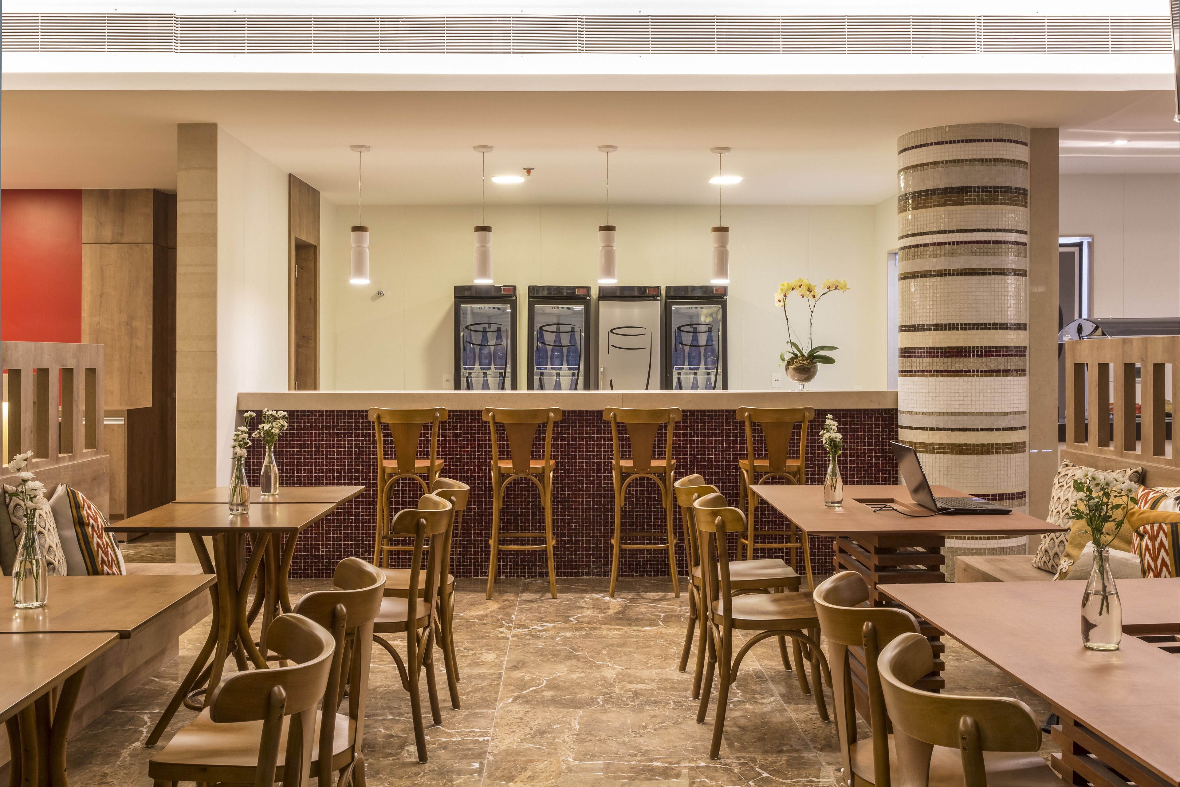 A modern restaurant with wooden tables and chairs, a bar area, and a decorative column.