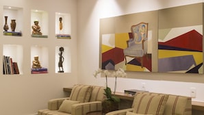 A lobby with two armchairs, a bookshelf with books and decorative items, and abstract paintings on the wall. - Sleep Inn Vit ória Praia do Canto (Vitoria)