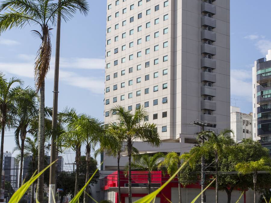 Un edificio de hotel alto con varios pisos y balcones, rodeado de palmeras y un cielo despejado.