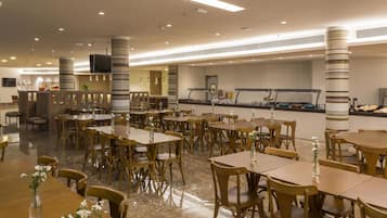 Un comedor amplio con varias mesas y sillas, una barra de buffet y un televisor montado en la pared.