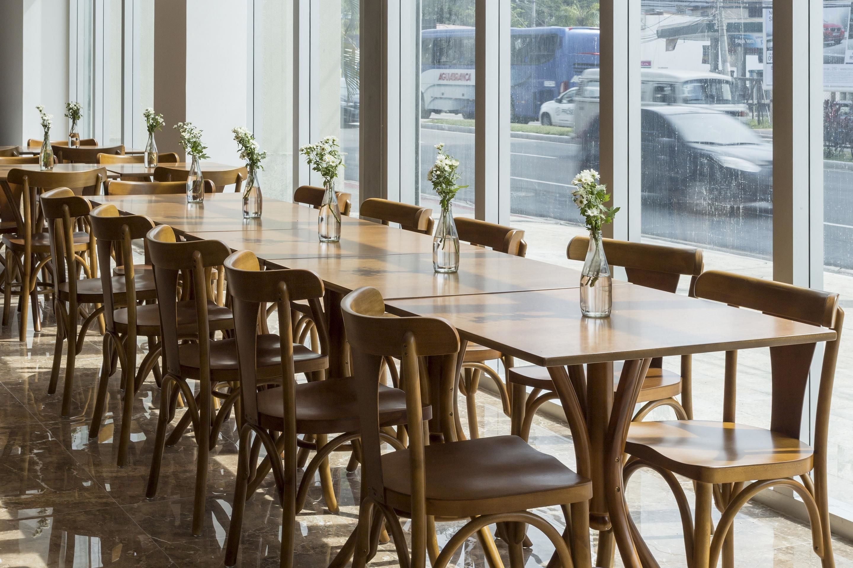 A restaurant with wooden tables and chairs, large windows, and vases with flowers.