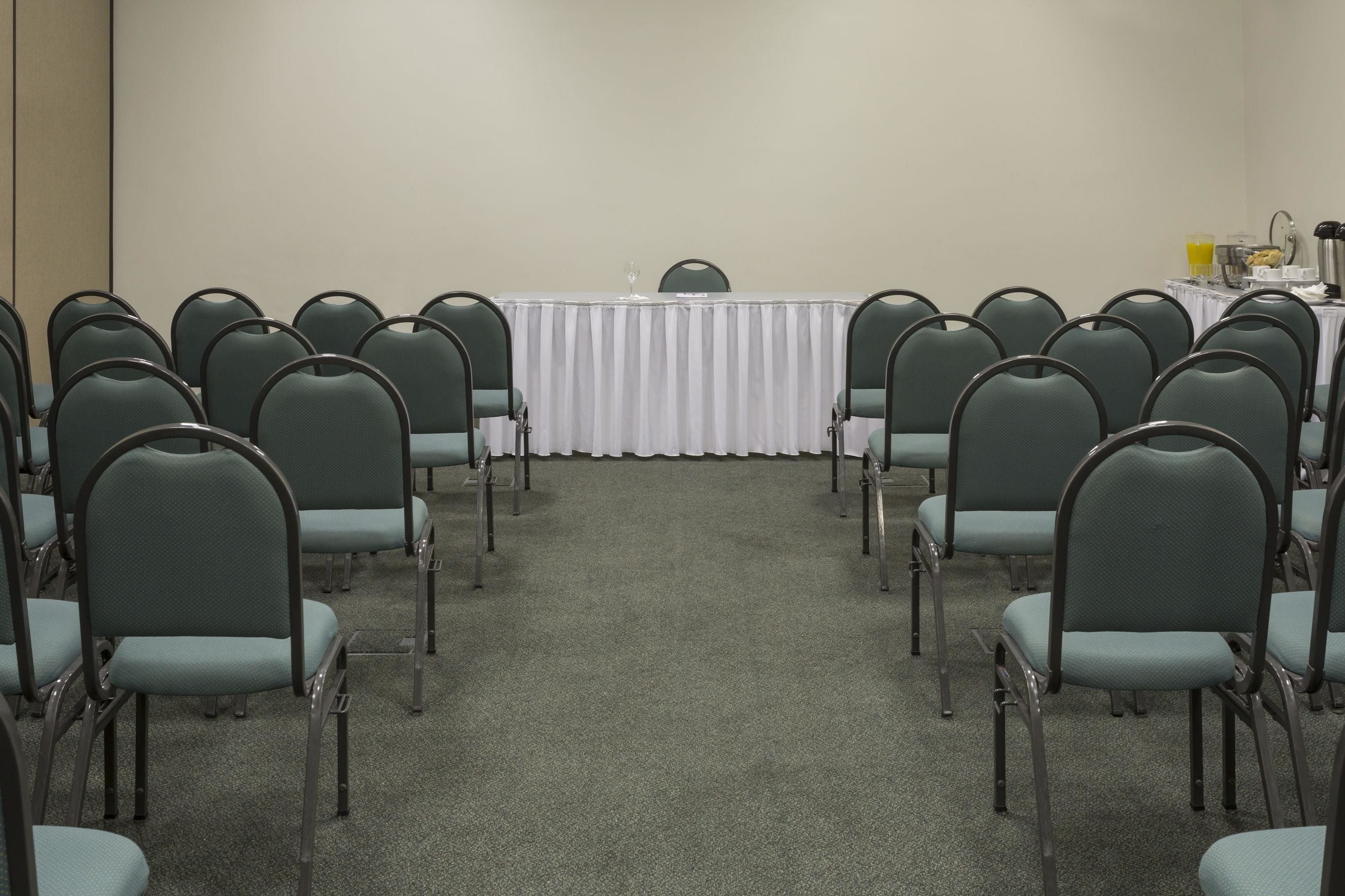 Un salón de conferencias con filas de sillas mirando una mesa cubierta con un mantel blanco.