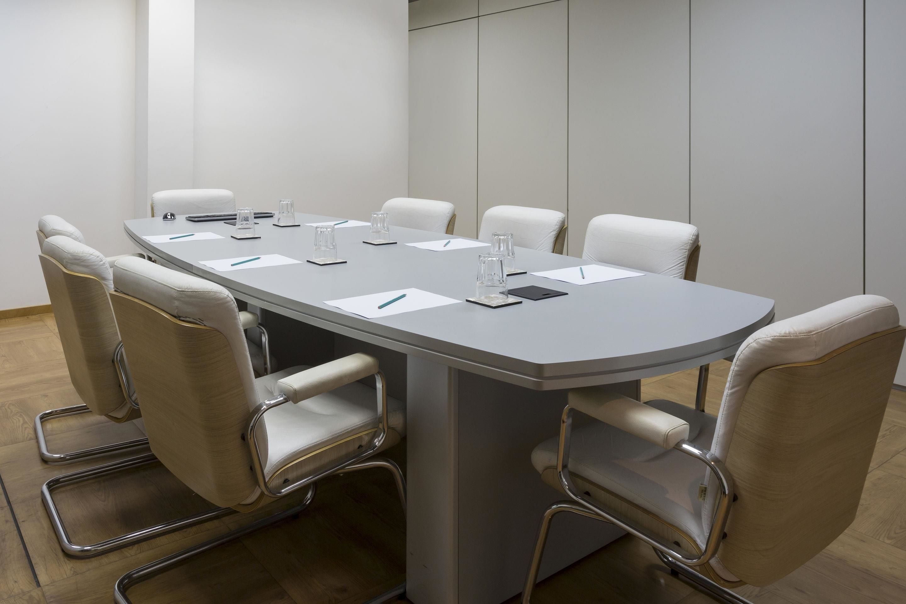 Uma sala de conferências com uma mesa retangular, seis cadeiras brancas e esquema de cores neutras.