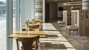 A modern hotel lobby with long tables and chairs, large windows, and a central column. - Sleep Inn Vitória Praia do Canto (Vitoria)