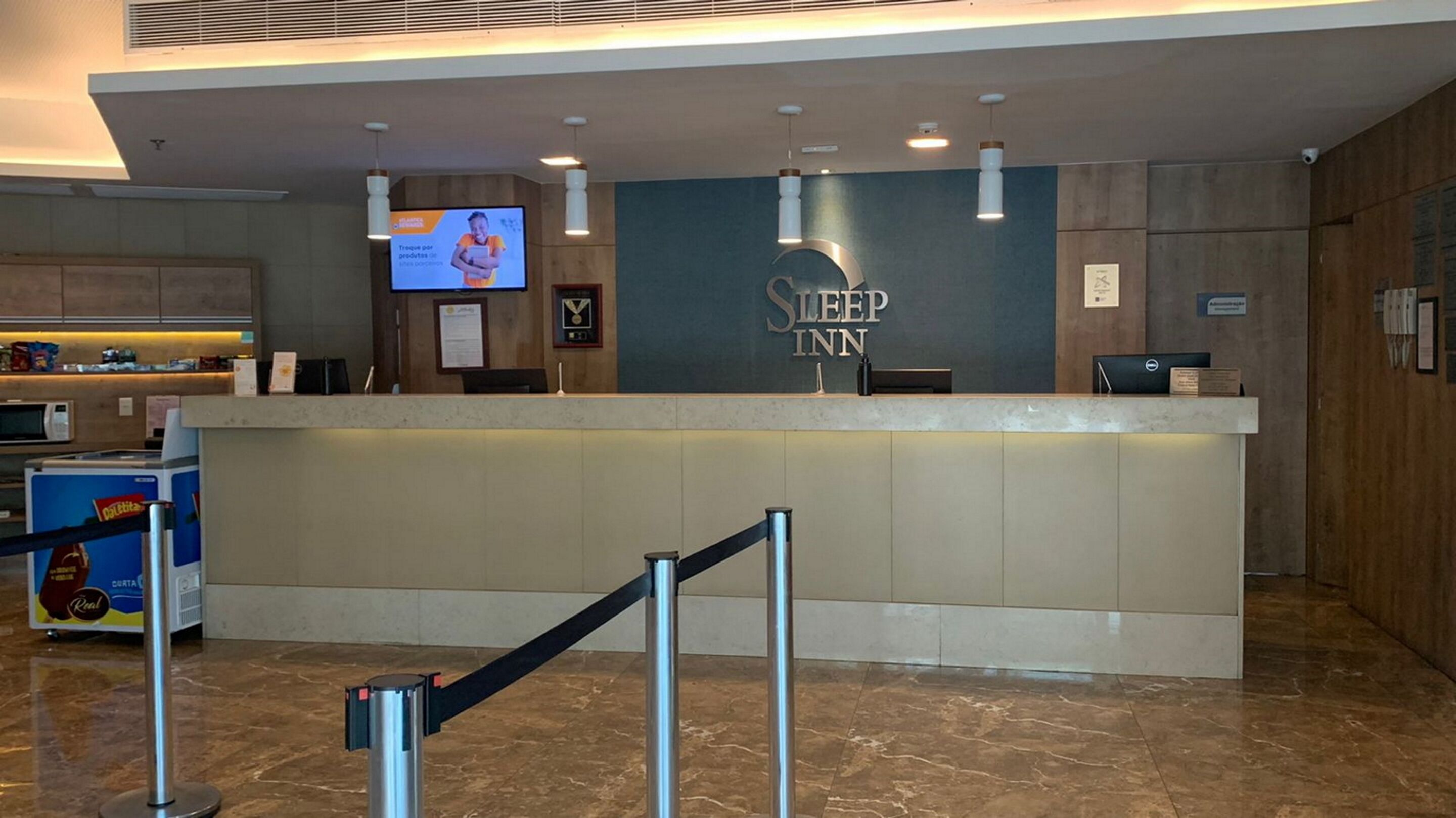 A reception desk with a sign reading "Sleep Inn" and a television screen displaying an advertisement.