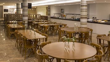 Un amplio comedor con varias mesas y sillas redondas, una barra de buffet y pilares decorativos.