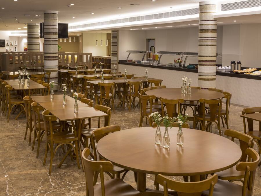 Un amplio comedor con varias mesas y sillas redondas, una barra de buffet y pilares decorativos.