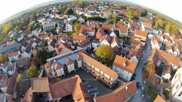 An aerial view of a residential area with houses, streets, and a central building with a red roof.