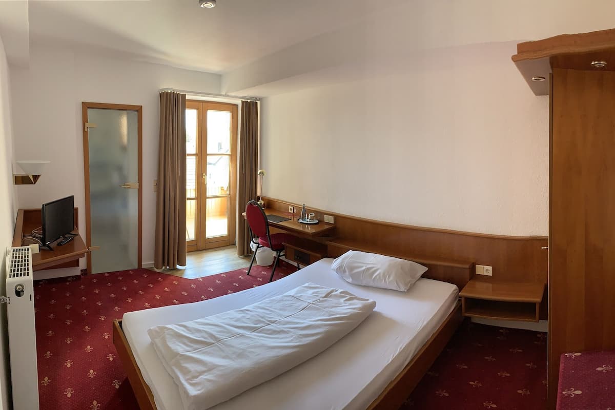 A hotel room with a bed, a desk with a chair, a TV, and a window with curtains.