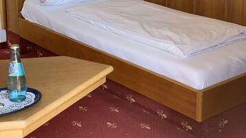 Una cama individual con cabecera de madera, una mesita de noche con una botella y un vaso, y una lámpara fijada a la pared.