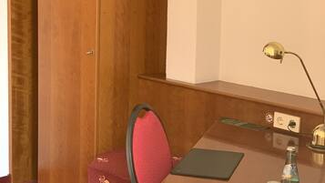 Una habitación pequeña con un escritorio de madera, una silla, una lámpara de escritorio y una botella de agua sobre la mesa.