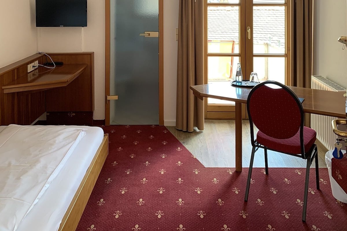 A hotel room with a bed, a desk, a chair, a television, and a window with curtains.