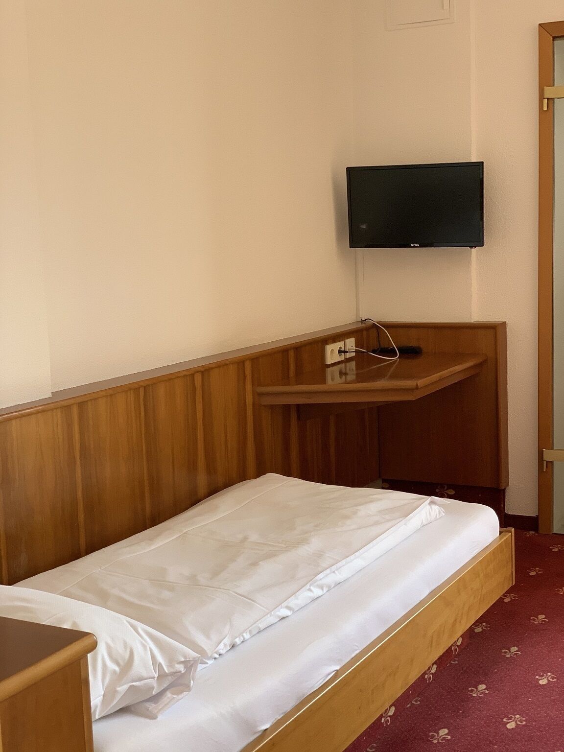 A single bed with a wooden headboard, a bedside table, and a mounted television on the wall.