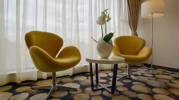 A room with two yellow armchairs, a white vase with an orchid, a small round table, and a patterned carpet.
