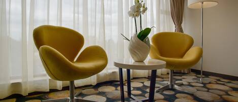 A room with two yellow armchairs, a white vase with an orchid, a small round table, and a patterned carpet.