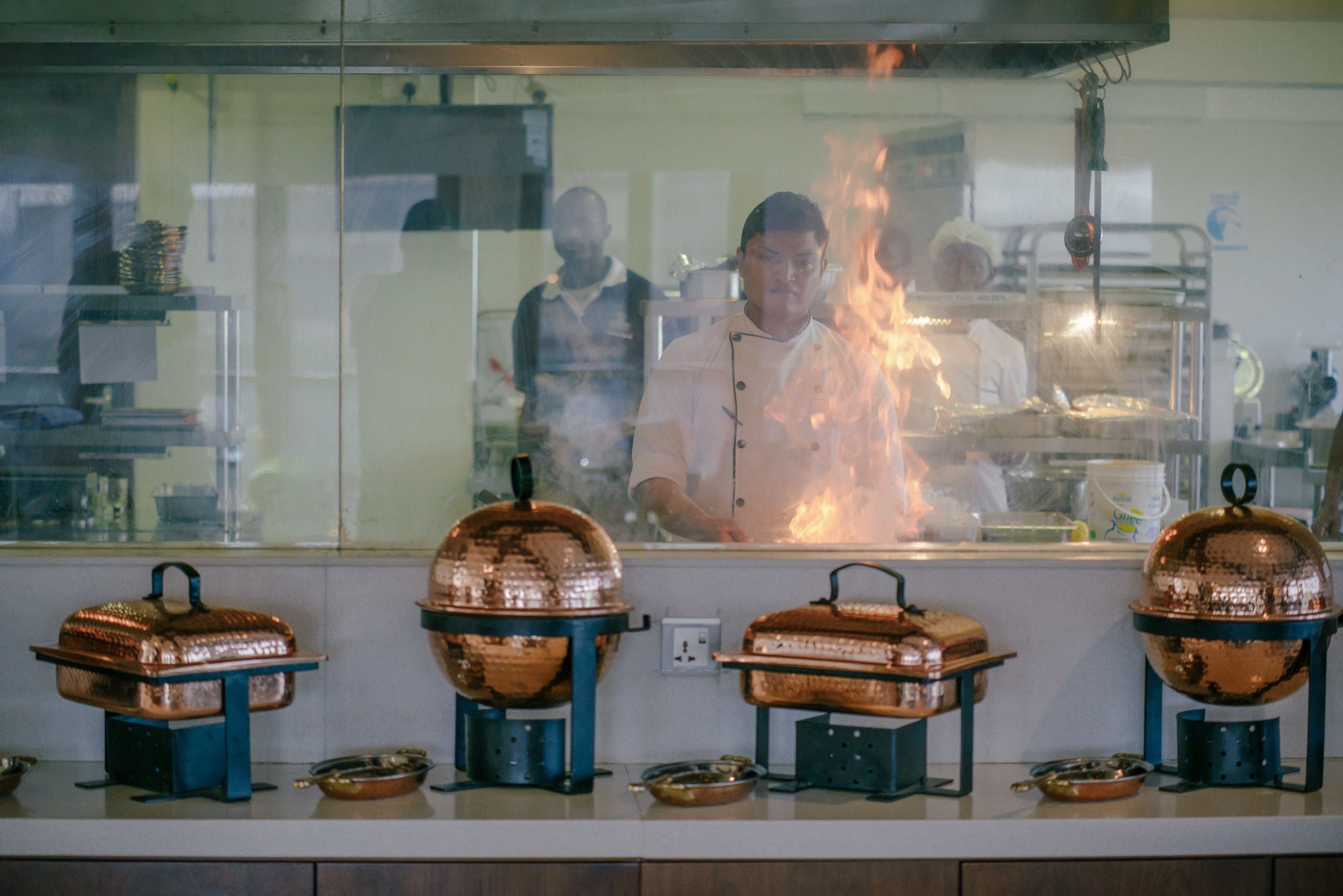 Una cocina con utensilios de cobre y un chef trabajando detrás de un separador de vidrio.