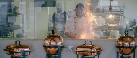 A kitchen with copper cooking equipment and a chef working behind a glass partition.